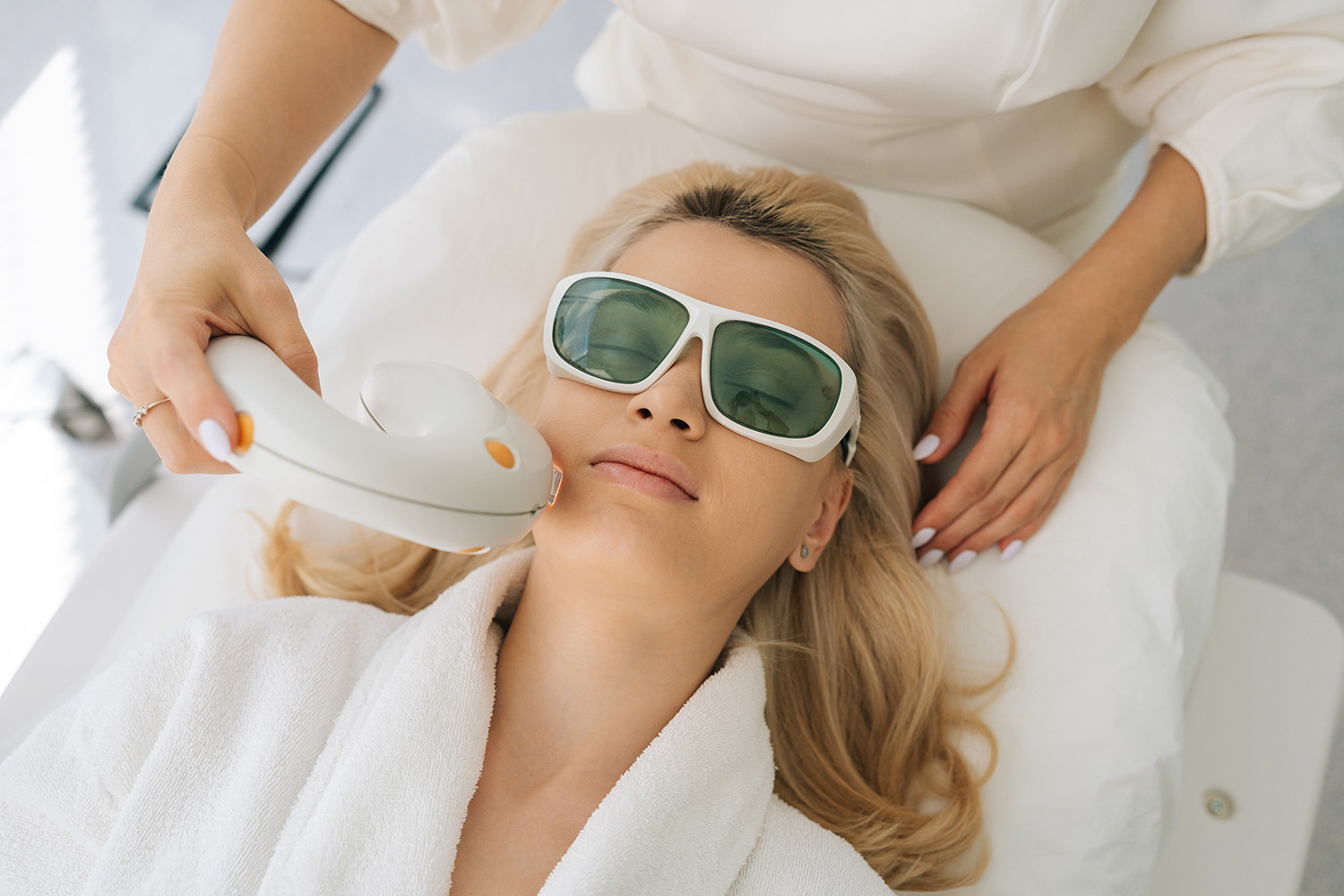 blonde young woman with protective glasses getting photo rejuvenation procedure