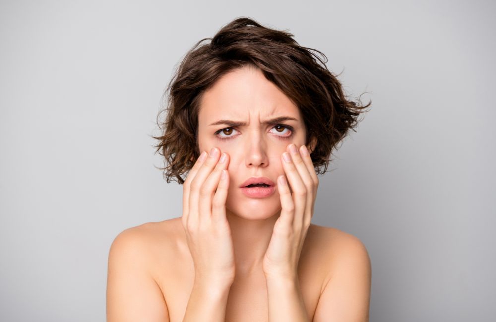 Smiling woman with glowing skin gently touching her face, representing facial treatments in Costa Mesa.