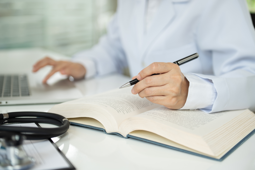 Doctor taking notes and researching clinical trial data at a desk.