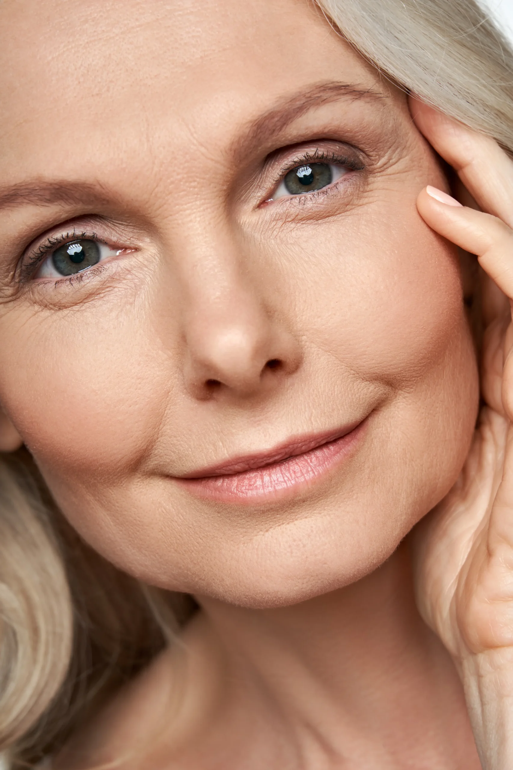 Close-up portrait of a woman touching the side of her face with visible fine lines around the eyes.