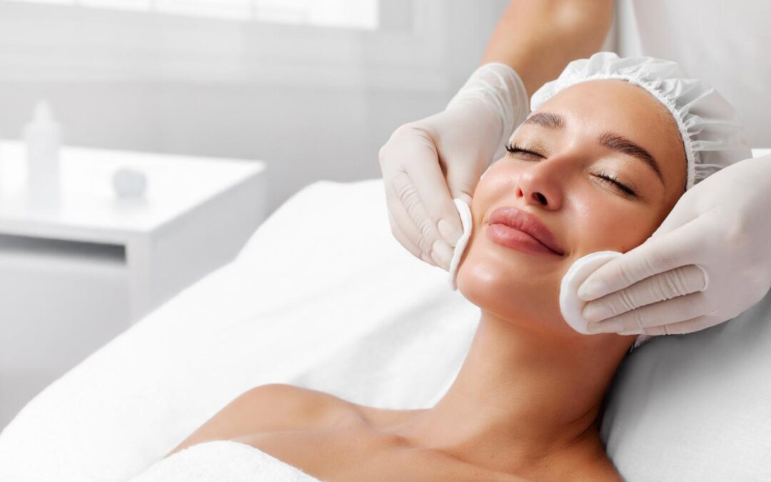Woman lies on a treatment bed while gloved hands hold round pads against both sides of her face.