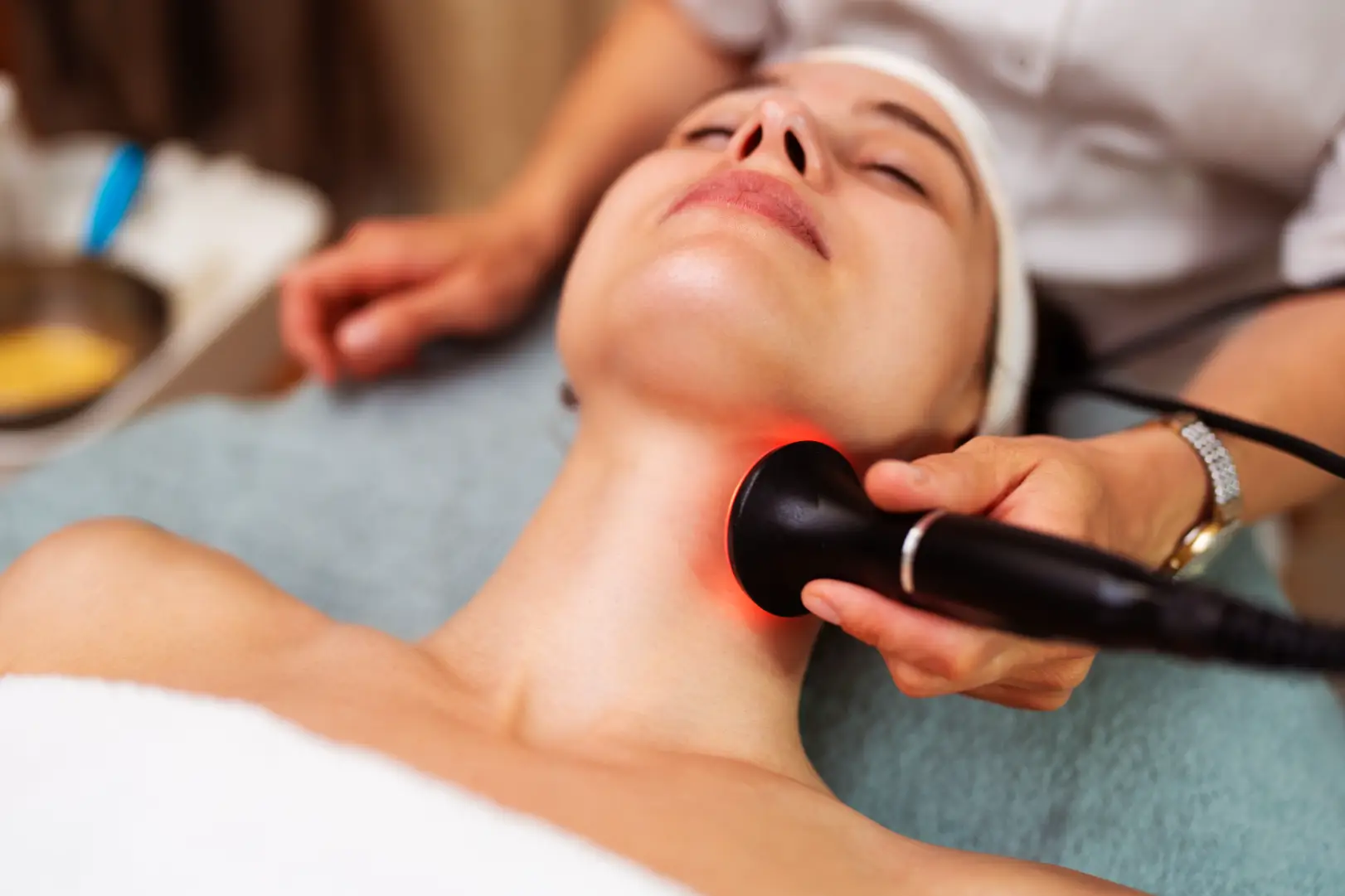 Person lying down while a handheld device with red light touches the side of the neck.