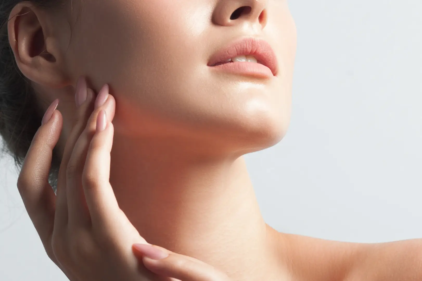 Close-up of a woman's jawline and neck with fingers touching the side of her face.